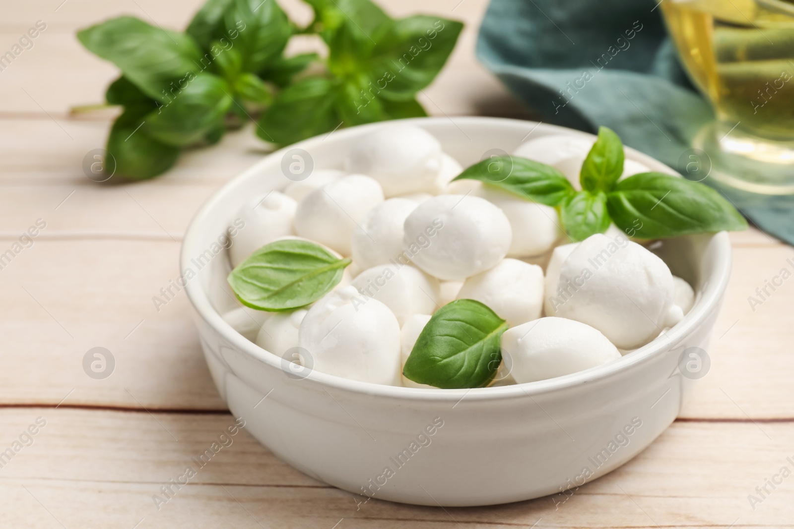 Tasty mozzarella cheese balls in bowl and basil on light wooden table, closeup Photo of Tasty mozzarella cheese balls in bowl and basil on light wooden table, closeup