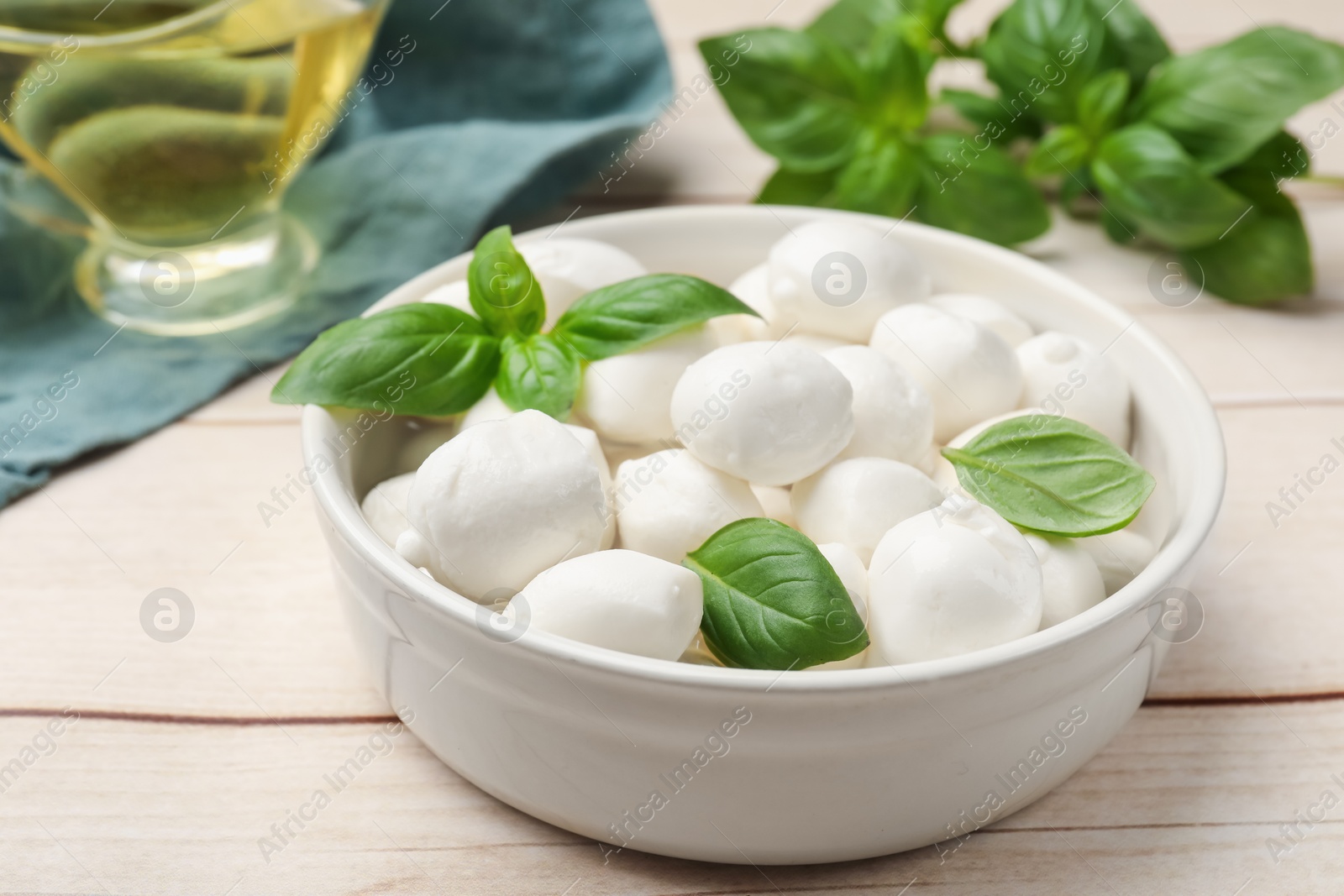 Tasty mozzarella cheese balls in bowl and basil on light wooden table, closeup Photo of Tasty mozzarella cheese balls in bowl and basil on light wooden table, closeup
