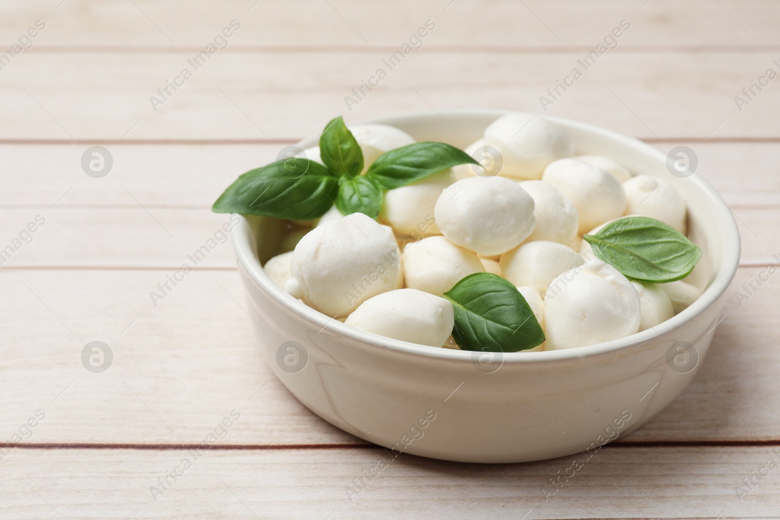 Tasty mozzarella cheese balls in bowl and basil on light wooden table, closeup. Space for text Photo of Tasty mozzarella cheese balls in bowl and basil on light wooden table, closeup. Space for text
