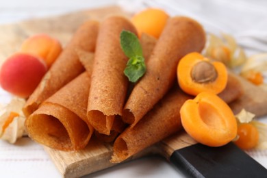 Photo of Delicious fruit leather rolls, apricots and physalis on white wooden table, closeup