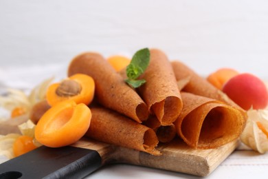 Photo of Delicious fruit leather rolls, apricots and physalis on white wooden table, closeup