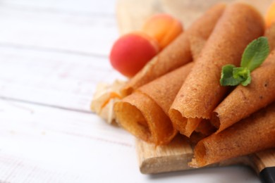 Photo of Delicious fruit leather rolls and apricots on white wooden table, closeup. Space for text