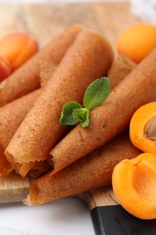 Photo of Delicious fruit leather rolls and apricots on white wooden table, closeup