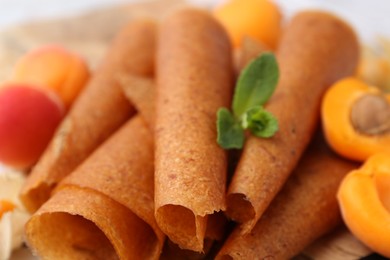 Photo of Delicious fruit leather rolls and apricots on table, closeup