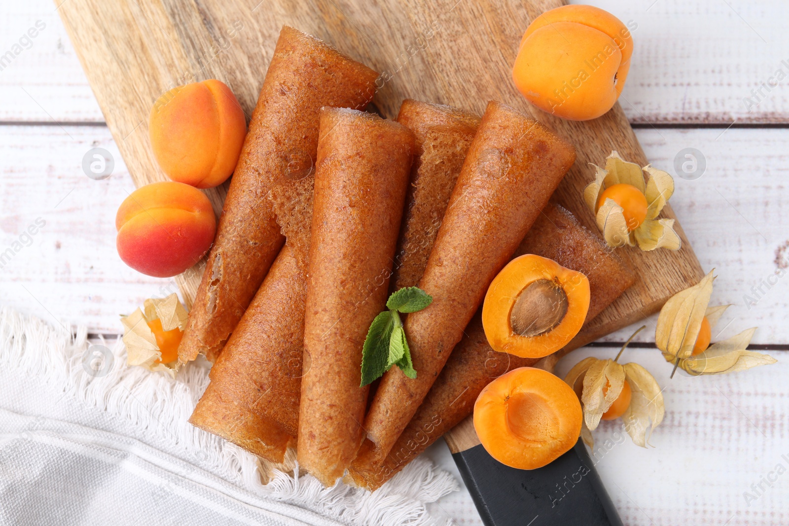 Delicious fruit leather rolls, apricots and physalis on white wooden table, flat lay Photo of Delicious fruit leather rolls, apricots and physalis on white wooden table, flat lay