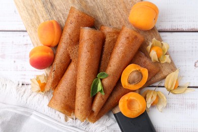 Photo of Delicious fruit leather rolls, apricots and physalis on white wooden table, flat lay