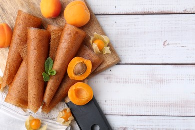 Photo of Delicious fruit leather rolls, apricots and physalis on white wooden table, flat lay. Space for text