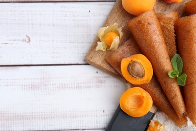 Photo of Delicious fruit leather rolls, apricots and physalis on white wooden table, flat lay. Space for text