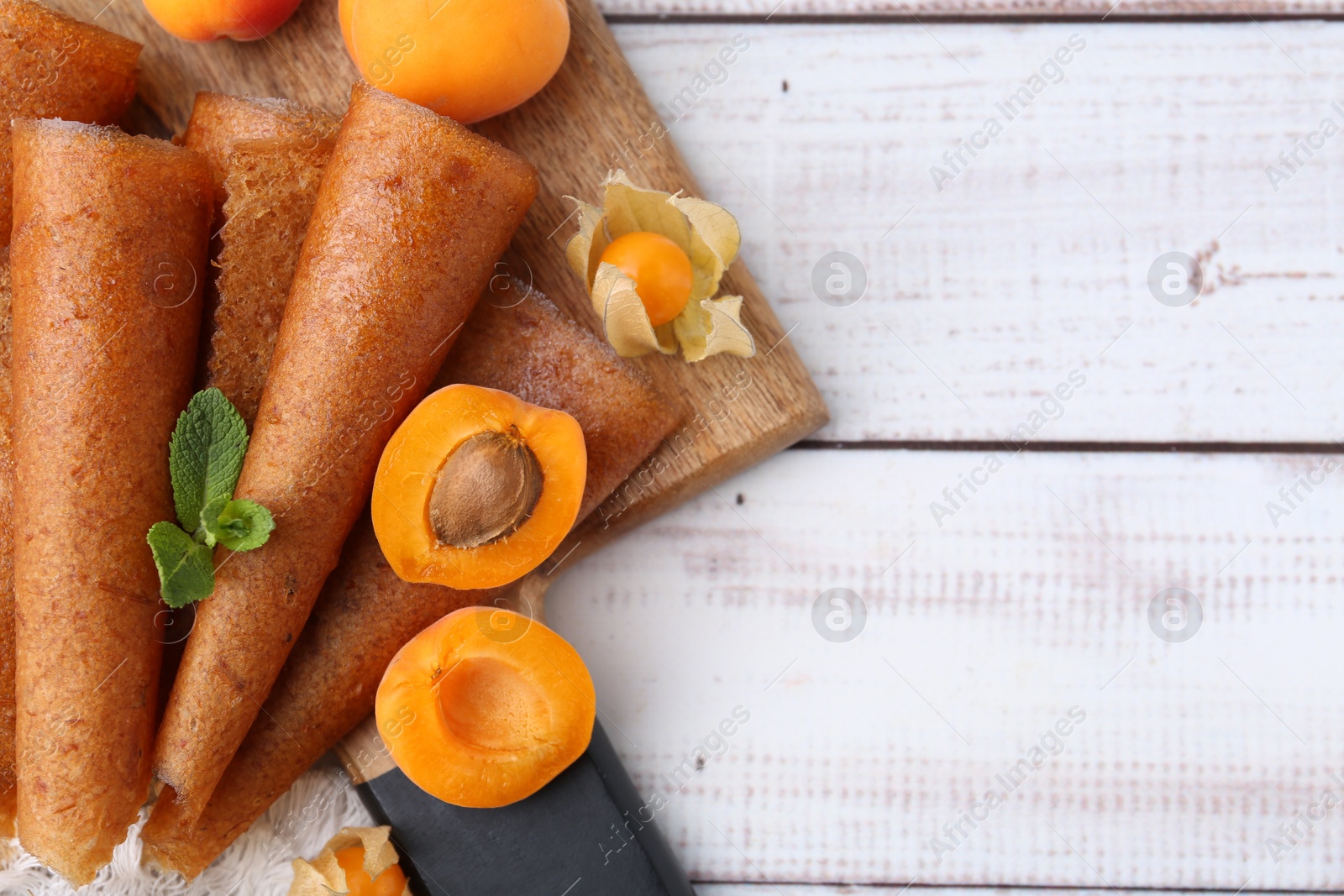 Delicious fruit leather rolls, apricots and physalis on white wooden table, flat lay. Space for text Photo of Delicious fruit leather rolls, apricots and physalis on white wooden table, flat lay. Space for text