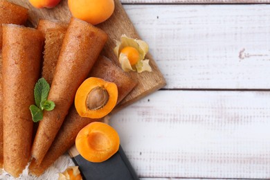 Photo of Delicious fruit leather rolls, apricots and physalis on white wooden table, flat lay. Space for text