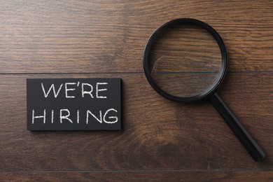 Image of We Are Hiring. Paper cards and magnifying glass on wooden table, top view. Recruitment, human resources concept
