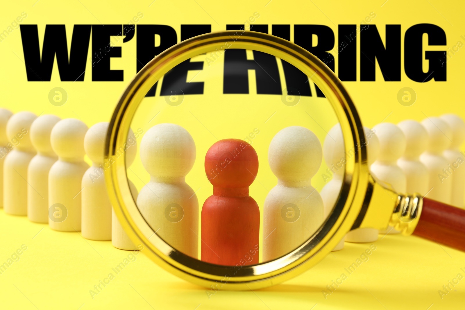 We Are Hiring. Red figure among wooden ones on yellow background, view through magnifying glass. Recruitment, human resources concept Image of We Are Hiring. Red figure among wooden ones on yellow background, view through magnifying glass. Recruitment, human resources concept