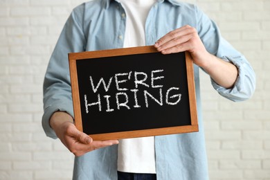 Image of Woman holding small blackboard with phrase We Are Hiring indoors, closeup. Recruitment, human resources concept