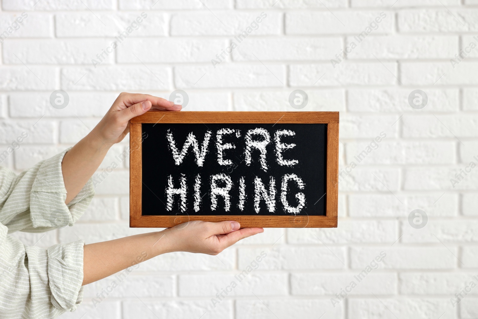 Woman holding small blackboard with phrase We Are Hiring against white brick wall, closeup. Recruitment, human resources concept Image of Woman holding small blackboard with phrase We Are Hiring against white brick wall, closeup. Recruitment, human resources concept