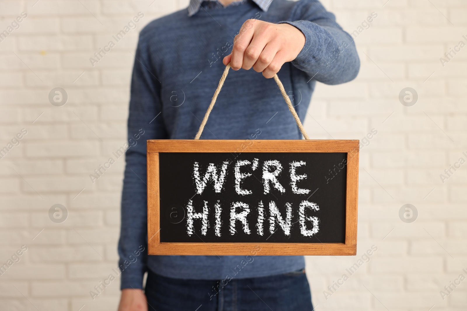 Man holding small blackboard with phrase We Are Hiring indoors, closeup. Recruitment, human resources concept Image of Man holding small blackboard with phrase We Are Hiring indoors, closeup. Recruitment, human resources concept