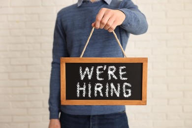 Image of Man holding small blackboard with phrase We Are Hiring indoors, closeup. Recruitment, human resources concept