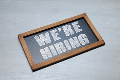 Image of Small blackboard with phrase We Are Hiring on grey wooden background. Recruitment, human resources concept