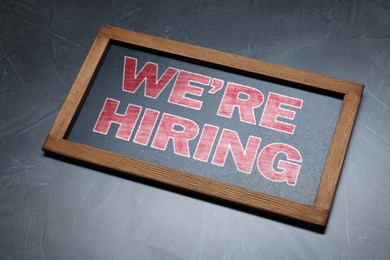 Image of Small blackboard with phrase We Are Hiring on grey textured background. Recruitment, human resources concept