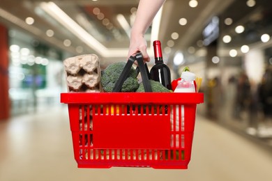 Image of Woman holding shopping basket with different food products at supermarket, closeup