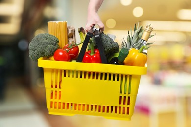 Image of Woman holding shopping basket with different food products at supermarket, closeup