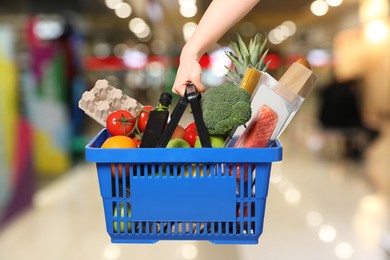 Image of Woman holding shopping basket with different food products at supermarket, closeup