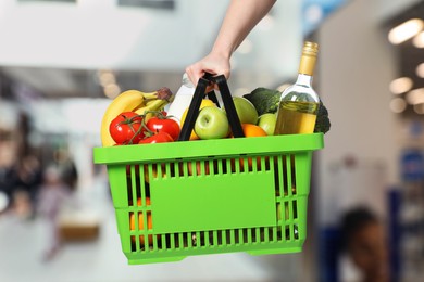 Image of Woman holding shopping basket with different food products at supermarket, closeup