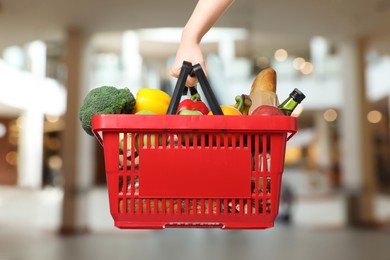 Image of Woman holding shopping basket with different food products at supermarket, closeup