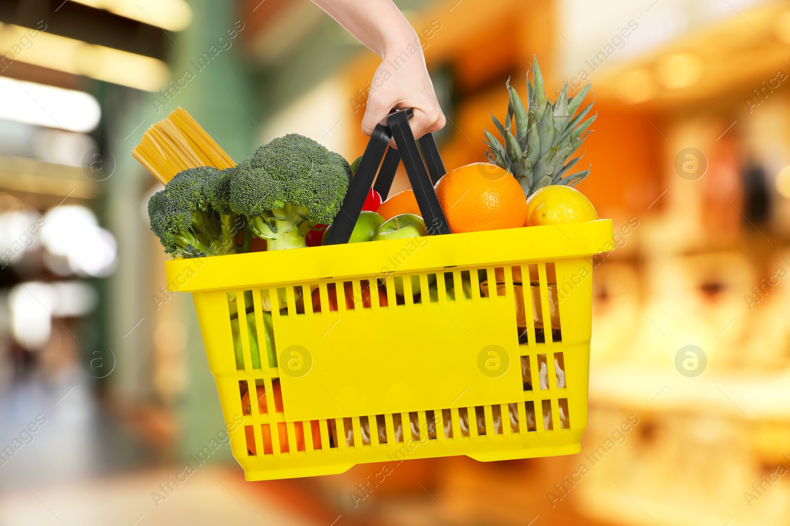 Woman holding shopping basket with different food products at supermarket, closeup Image of Woman holding shopping basket with different food products at supermarket, closeup