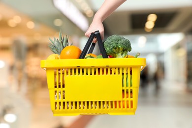 Image of Woman holding shopping basket with different food products at supermarket, closeup