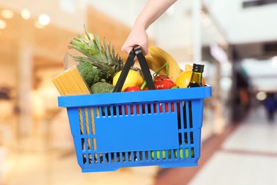 Image of Woman holding shopping basket with different food products at supermarket, closeup