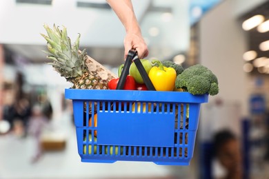 Image of Man holding shopping basket with different food products at supermarket, closeup