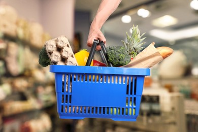 Image of Man holding shopping basket with different food products at supermarket, closeup