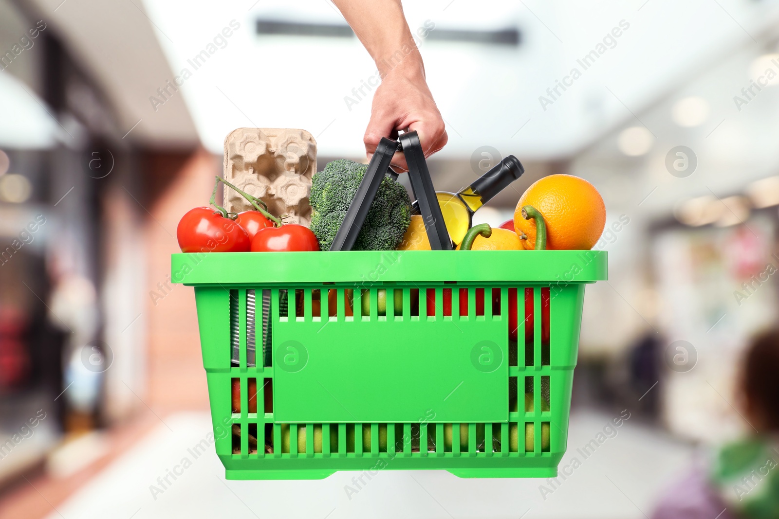 Man holding shopping basket with different food products at supermarket, closeup Image of Man holding shopping basket with different food products at supermarket, closeup