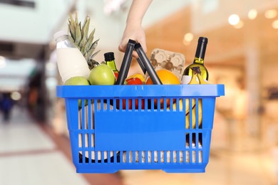 Image of Woman holding shopping basket with different food products at supermarket, closeup