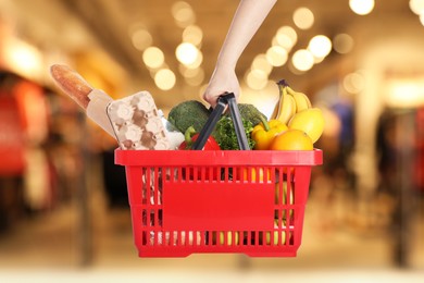 Image of Woman holding shopping basket with different food products at supermarket, closeup