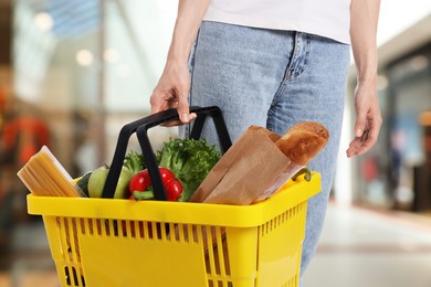 Image of Woman holding shopping basket with different food products at supermarket, closeup