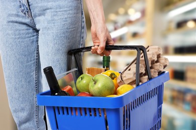 Image of Woman holding shopping basket with different food products at supermarket, closeup