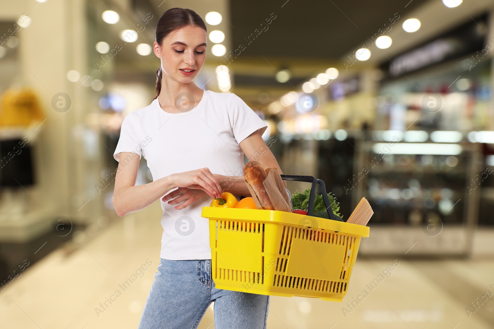 Image of Woman holding shopping basket with different food products at supermarket