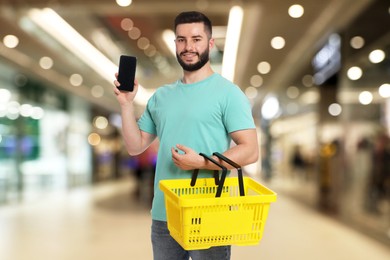Image of Man holding empty shopping basket and mobile phone at supermarket