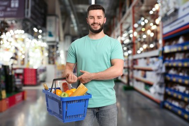 Image of Man holding shopping basket with different food products at supermarket