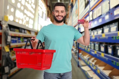 Image of Man holding empty shopping basket and bank card at supermarket