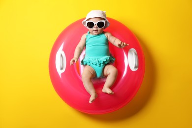 Photo of Cute little baby in sunglasses with inflatable ring on yellow background
