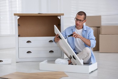Photo of Man assembling furniture with screwdriver on floor at home