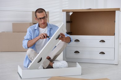 Photo of Man assembling furniture with screwdriver on floor at home