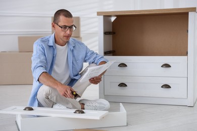 Photo of Man with manual and screwdriver assembling furniture on floor at home