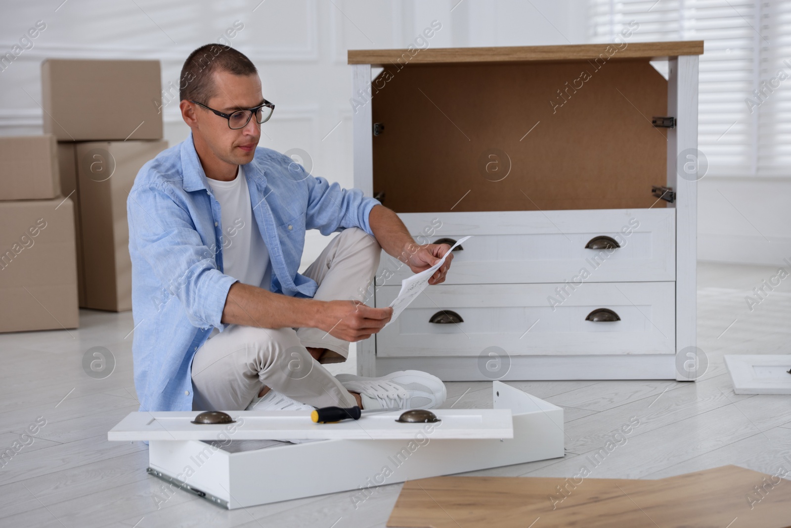 Man with manual and screwdriver assembling furniture on floor at home Photo of Man with manual and screwdriver assembling furniture on floor at home