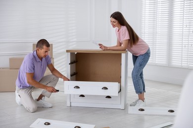 Photo of Happy couple with manual assembling furniture on floor at home