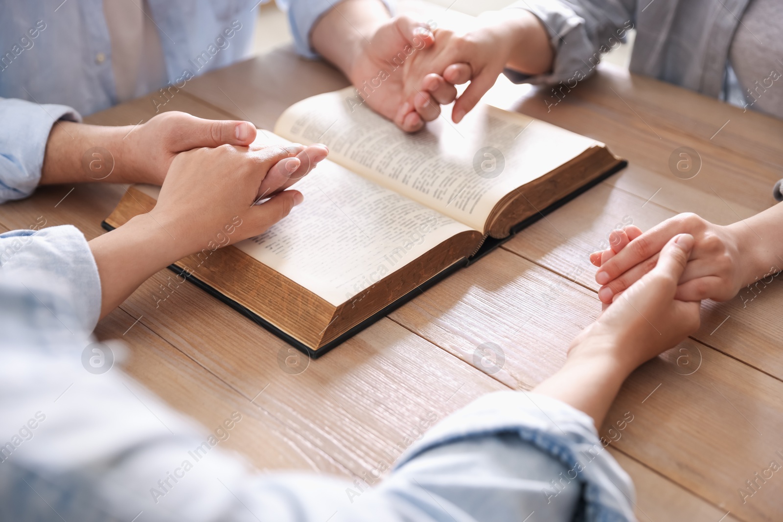 Family with Bible praying at wooden table indoors, closeup Photo of Family with Bible praying at wooden table indoors, closeup