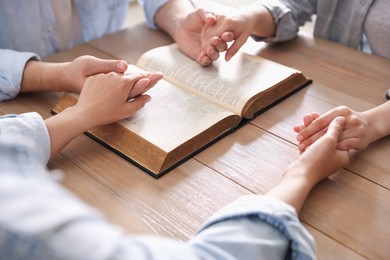 Photo of Family with Bible praying at wooden table indoors, closeup