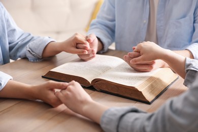 Photo of Family with Bible praying at wooden table indoors, closeup